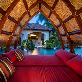 Expansive tropical backyard custom-shaped natural pool in San Diego with natural stone pavers and a pool house.