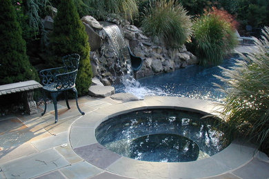 Imagen de piscina con fuente natural clásica grande redondeada en patio trasero con adoquines de piedra natural
