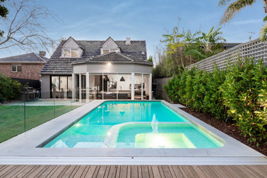 Modelo de piscina actual de tamaño medio a medida en patio trasero con paisajismo de piscina y losas de hormigón