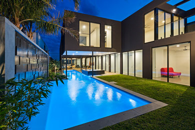 Modelo de piscinas y jacuzzis alargados actuales grandes en forma de L en patio trasero con adoquines de hormigón