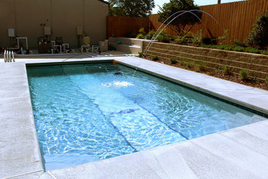 Imagen de piscina con fuente alargada grande rectangular en patio trasero con adoquines de hormigón