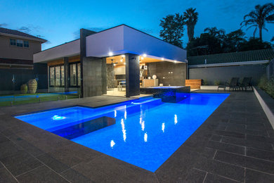 Modelo de piscinas y jacuzzis alargados contemporáneos grandes en forma de L en patio trasero con adoquines de hormigón