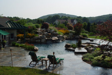 Exempel på en mycket stor klassisk anpassad pool på baksidan av huset, med en fontän och naturstensplattor