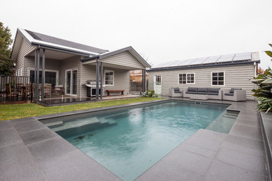 Modelo de piscina alargada de tamaño medio rectangular en patio trasero con adoquines de hormigón