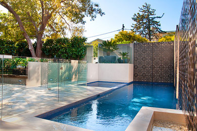 Imagen de piscina moderna de tamaño medio en forma de L en patio trasero con adoquines de piedra natural