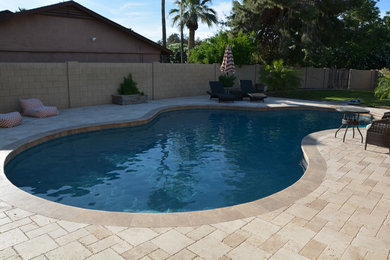 Foto de piscina tradicional de tamaño medio tipo riñón en patio trasero con adoquines de piedra natural