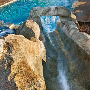 Immagine di una piscina tropicale rettangolare di medie dimensioni e dietro casa con un acquascivolo e lastre di cemento