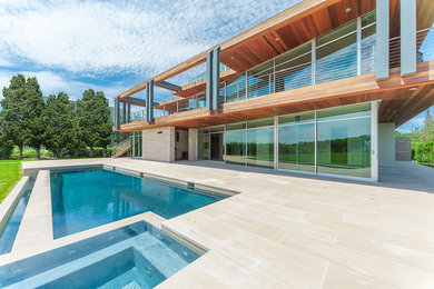 Modelo de piscina alargada contemporánea rectangular en patio trasero con adoquines de piedra natural