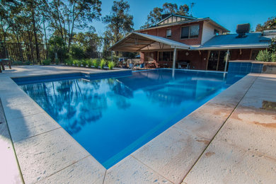 Diseño de piscina infinita campestre de tamaño medio rectangular en patio trasero con adoquines de hormigón
