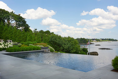 Example of a large classic backyard stone and rectangular infinity pool fountain design in New York