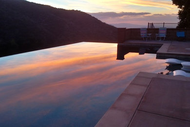 This is an example of a large contemporary back rectangular infinity hot tub in Los Angeles with concrete paving.