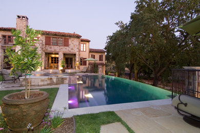 Esempio di una grande piscina a sfioro infinito rustica rettangolare dietro casa con fontane e pavimentazioni in pietra naturale