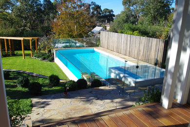 Large modern back rectangular above ground swimming pool in Melbourne with natural stone paving.