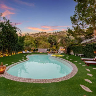 Photo of a large mediterranean backyard kidney-shaped natural pool in Los Angeles with a pool house and brick pavers.