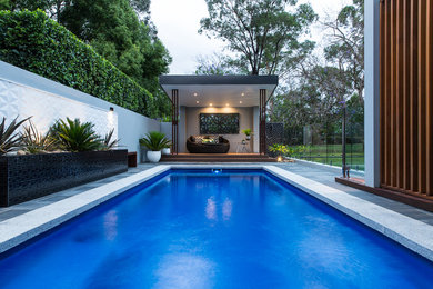 Foto de piscina actual grande rectangular en patio trasero con adoquines de piedra natural