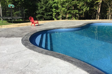 Cette image montre une grande piscine arrière design en forme de haricot avec du béton estampé.