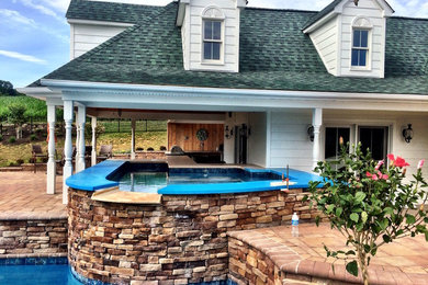 Diseño de piscina con fuente infinita costera grande a medida en patio trasero con adoquines de hormigón