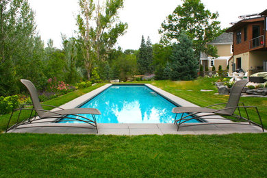 Modelo de piscina alargada moderna grande rectangular en patio trasero con adoquines de hormigón