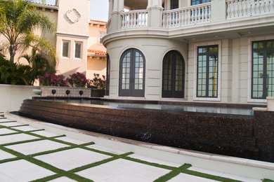 Immagine di un'ampia piscina a sfioro infinito minimal personalizzata dietro casa con pavimentazioni in cemento