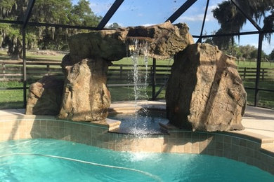 Ejemplo de piscina con fuente alargada tropical grande tipo riñón en patio trasero con losas de hormigón