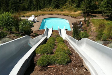 Idee per una grande piscina minimalista rettangolare dietro casa con un acquascivolo e lastre di cemento
