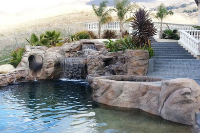 Idee per una grande piscina a sfioro infinito design personalizzata dietro casa con un acquascivolo e pavimentazioni in pietra naturale