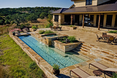 Diseño de piscina con fuente alargada rural grande a medida en patio trasero con losas de hormigón
