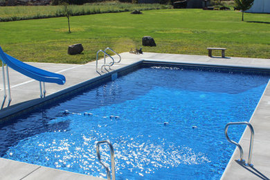 Diseño de piscina con tobogán tradicional grande rectangular en patio trasero con suelo de hormigón estampado