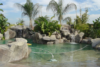 Ejemplo de piscina con fuente elevada grande a medida en patio trasero con suelo de hormigón estampado