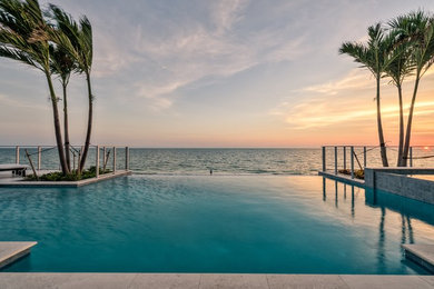 Design ideas for an expansive beach style back rectangular infinity swimming pool in Miami with a water feature and natural stone paving.