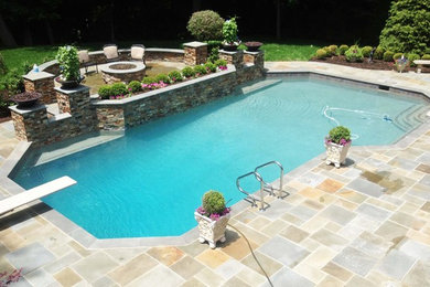 Photo of a large classic back custom shaped lengths swimming pool in Detroit with natural stone paving.