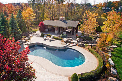 Large traditional back custom shaped natural swimming pool in Detroit with concrete paving and a pool house.