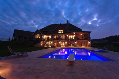 Ejemplo de piscina alargada de estilo de casa de campo grande rectangular en patio trasero con adoquines de hormigón