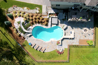 Klassisk inredning av en stor anpassad pool på baksidan av huset, med vattenrutschkana och naturstensplattor