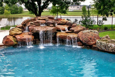 Large modern back custom shaped swimming pool in Houston with a water feature and stamped concrete.