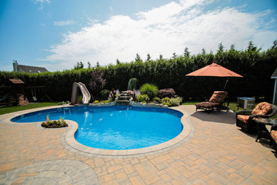 Foto de piscina con tobogán tipo riñón en patio trasero con adoquines de ladrillo