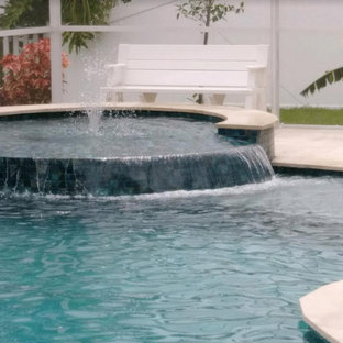 Immagine di una piscina monocorsia tropicale a "L" di medie dimensioni e dietro casa con una vasca idromassaggio e pavimentazioni in cemento