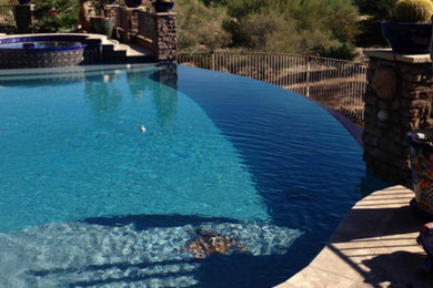 Inspiration for a large contemporary back custom shaped infinity hot tub in Phoenix with stamped concrete.