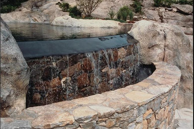 Ejemplo de piscina natural tropical grande a medida en patio trasero con adoquines de piedra natural