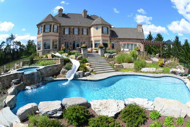 Ejemplo de piscina con tobogán actual grande a medida en patio trasero con adoquines de piedra natural