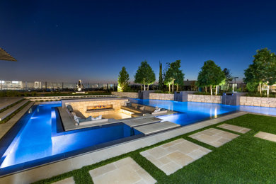 Esempio di un'ampia piscina a sfioro infinito minimalista personalizzata dietro casa con fontane e pavimentazioni in pietra naturale