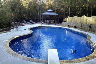 Modelo de piscina natural tropical grande a medida en patio trasero con suelo de hormigón estampado