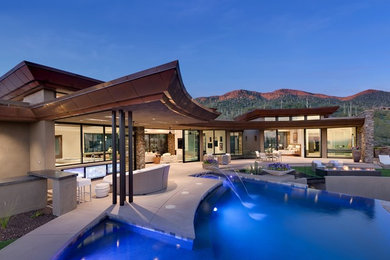 Diseño de piscina infinita actual grande a medida en patio trasero con adoquines de hormigón