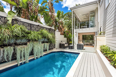 Imagen de piscina alargada tropical rectangular en patio lateral con entablado