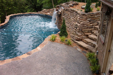 Modelo de piscina con fuente natural rústica grande a medida en patio trasero con suelo de hormigón estampado