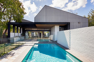 Diseño de piscina natural actual de tamaño medio rectangular en patio trasero con adoquines de piedra natural