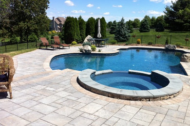 Diseño de piscina natural tradicional grande a medida en patio trasero con adoquines de hormigón