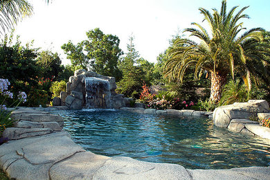 Ejemplo de piscina con fuente alargada exótica grande a medida en patio trasero con adoquines de piedra natural