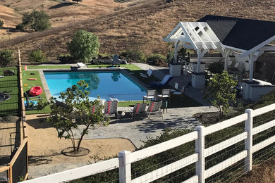 Ejemplo de piscina campestre extra grande rectangular en patio trasero con suelo de hormigón estampado