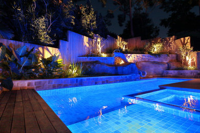 Imagen de piscina con tobogán alargada actual de tamaño medio rectangular en patio lateral con losas de hormigón